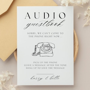以下が含まれることがあります： 「AUDIO guestbook」と書かれた黒い文字の白いカード。タイトルの下には「SORRY, WE CAN'T COME TO THE PHONE RIGHT NOW...」というフレーズがあります。中央には、ヴィンテージ電話の線画があります。カードには、指示と「harry & belle」という名前も含まれています。