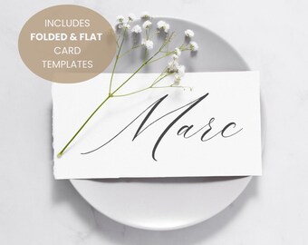 Könnte beinhalten: Eine weiße Tischkarte mit dem Namen "Marc" in eleganter schwarzer Schrift, auf einem grauen Teller. Zarte weiße Blumen und der Text "INCLUDES FOLDED & FLAT CARD TEMPLATES" in einem beigen Kreis.