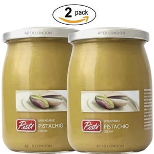 May include: Two jars of pistachio cream with silver lids, labeled "Pisti Pistachio Cream." The jars are a light green color, with a label showing a pistachio nut. The text "Apex London" is printed on the lid and the bottom of the jar. The image is labeled "2 pack."