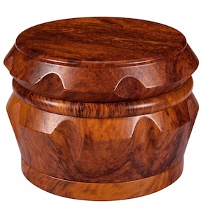 May include: A wooden grinder with a rich, dark brown finish. The grinder has a round, flat top and a cylindrical base with a series of angled, carved facets. The wood grain is visible throughout the design.