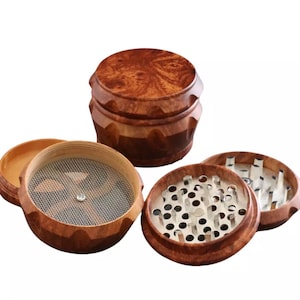 May include: A wooden herb grinder with multiple disassembled parts. The grinder is made of a dark brown wood with a natural grain pattern. The components include a top, a grinding chamber with metal teeth, a mesh screen, and a bottom chamber.