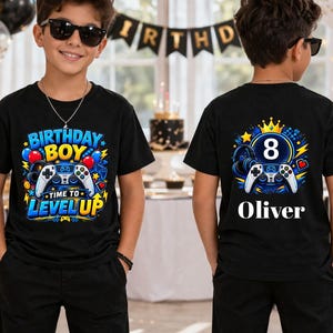 May include: A black t-shirt featuring a front graphic with a video game controller and the text "BIRTHDAY BOY TIME TO LEVEL UP" and a back graphic with a video game controller, the number "8", a crown, and the name "Oliver" in white text.