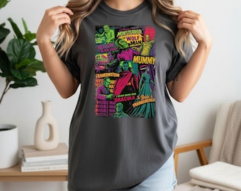 May include: Dark gray t-shirt featuring a colorful collage of classic monster movie characters. The graphic includes images of Frankenstein, Dracula, the Mummy, and the Wolf Man, with text like "Monsteror" and "Mummy".