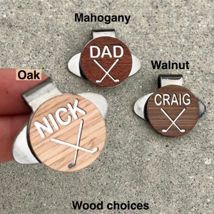 May include: Three golf ball markers with different wood choices: Oak, Mahogany, and Walnut. Each marker features a white name and crossed golf clubs. The names are "Nick", "Dad", and "Craig".