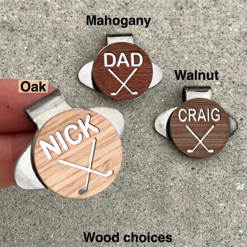 May include: Three golf ball markers with different wood choices: Oak, Mahogany, and Walnut. Each marker features a white name and crossed golf clubs. The names are "Nick", "Dad", and "Craig".