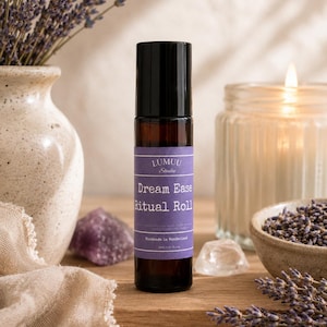 May include: A dark glass roll-on bottle with a black cap and a purple label that reads "Dream Ease Ritual Roll." The bottle is surrounded by lavender, a lit candle, and crystals. The label also says "Handmade in Wonderland."