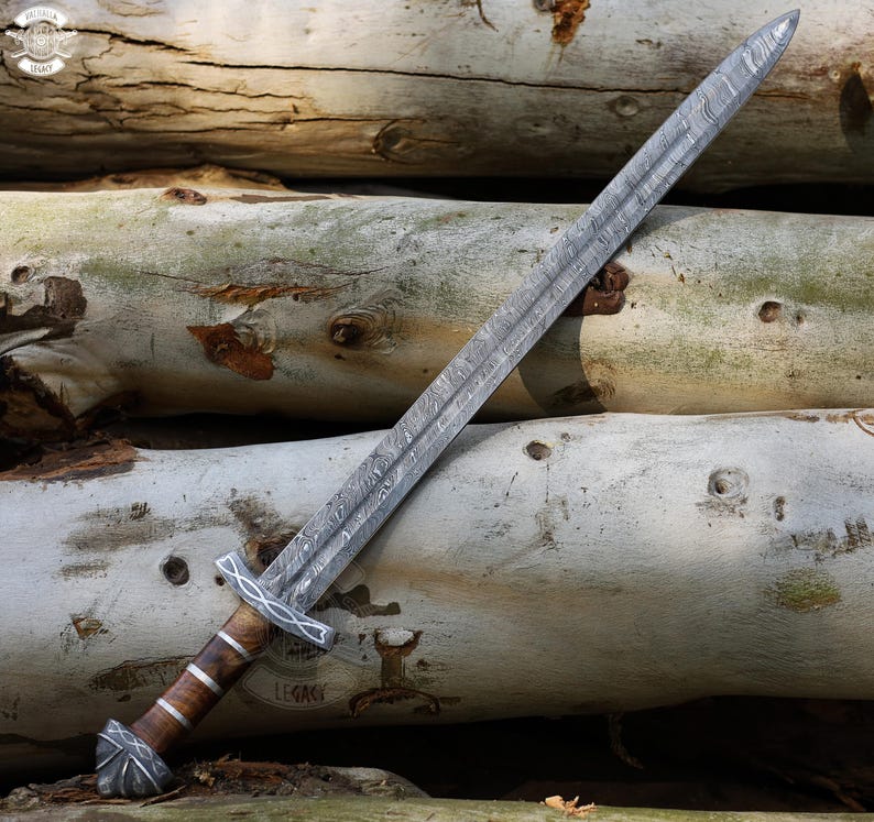 May include: A detailed image of a long sword with a patterned blade and a wooden handle. The sword's blade has a textured, wavy pattern. The handle is brown with silver accents. The sword is resting on a pile of logs.