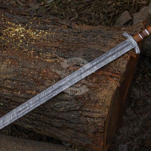 May include: A long, silver sword with a patterned blade and a wooden handle with metal accents. The sword is resting on a weathered, brown log. The image includes the text "Valhalla Legacy".