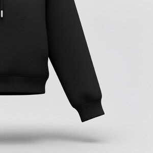 May include: A black hoodie with a ribbed hem and cuffs. The image shows a close-up of the sleeve and part of the body of the garment. The fabric appears to be a soft, medium-weight material.