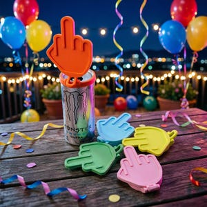 May include: A silver Monster Energy drink can with a bright orange silicone middle finger hand topper attached to the top. Four additional silicone hand toppers in light blue, yellow, green, and pink are arranged on the wooden surface.