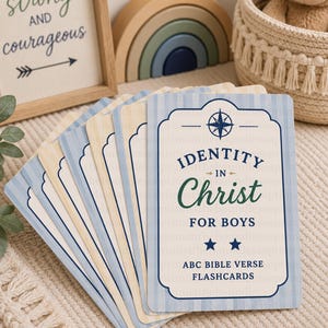 May include: A set of rectangular flashcards with a light blue and cream striped background. The top card features a compass icon, the text "IDENTITY IN Christ FOR BOYS", two blue stars, and the text "ABC BIBLE VERSE FLASHCARDS" in blue.