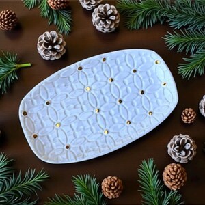 May include: An oval-shaped white ceramic serving platter featuring a repeating embossed geometric pattern of interconnected circles and ovals, accented with small, evenly spaced gold-colored dots at the center of each intersection.