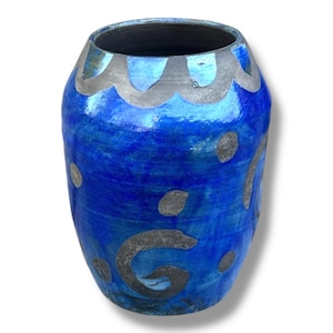 May include: A rounded ceramic vase with a glossy cobalt blue glaze. The exterior features hand-painted matte grey decorative elements, including a scalloped border around the top rim, scattered circular dots, and a prominent swirling spiral design.