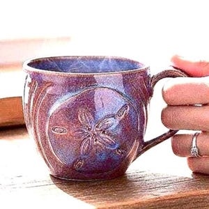 Taza de café con un dólar de arena esculpido en esmaltes óxido y azul