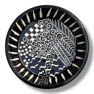Pode incluir: Prato de cerâmica preto com um design branco. O design apresenta uma variedade de padrões, incluindo espirais, pontos e linhas.