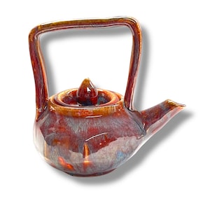 Może przedstawiać: Mały, czerwono-brązowy ceramiczny czajnik z pokrywką i uchwytem. Czajnik ma błyszczące wykończenie i unikalną, tęczową glazurę.