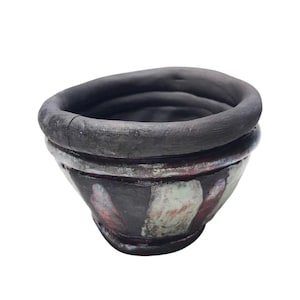 May include: A handmade ceramic bowl with a dark gray rim and a textured exterior. The bowl features a unique design with splashes of red, white, and green paint. The bowl is a decorative piece.