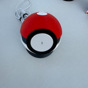 May include: A red and white wireless charger with a black band and a white charging surface. The charger has a lightning bolt symbol on the charging surface and a white USB-C cable.