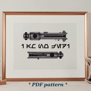 May include: Cross-stitch pattern of two lightsabers in shades of gray, with text in a stylized font. The framed artwork is displayed on a white background. The text at the bottom reads "* PDF pattern *".