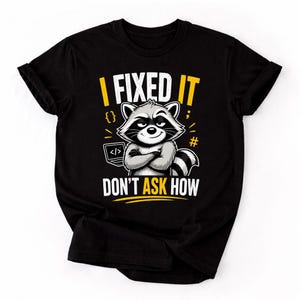 May include: Black t-shirt with a graphic of a raccoon with crossed arms and the text "I FIXED IT DON'T ASK HOW". The raccoon is gray and white, with a smug expression. The text is in yellow and white.