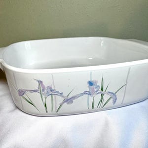 May include: White rectangular baking dish with handles, decorated with lavender and blue iris flowers and green leaves. The dish has a smooth, glossy finish and is suitable for baking and serving.