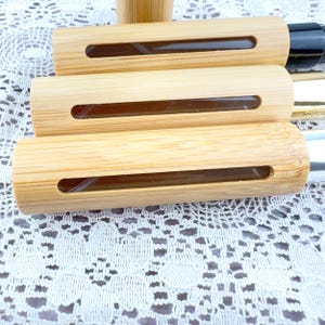 May include: Several bamboo essential oil roller bottles with a clear glass vial and a small opening. The bottles are cylindrical and have a natural wood grain finish. One bottle has a black cap.