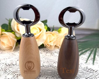 May include: Two bottle openers with wooden handles and metal tops. One handle is light-colored wood with a logo, the other is dark wood with the word "Test". The openers are displayed on a white lace surface with flowers in the background.