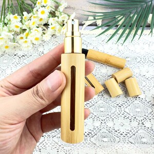 May include: A bamboo perfume atomizer with a gold-colored spray nozzle. The cylindrical bottle has a rectangular window to view the contents. Several bamboo caps and a longer bamboo tube are also visible.