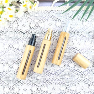 May include: Three bamboo-style perfume atomizers with different colored spray tops: black, gold, and silver. Each atomizer has a clear window and a matching bamboo cap. The atomizers are arranged on a white lace surface.