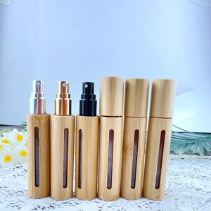 May include: A collection of bamboo spray bottles with various metal and black spray tops. The bottles have a clear window to view the contents. The bamboo has a natural wood grain finish. The bottles are designed for essential oils or perfumes.