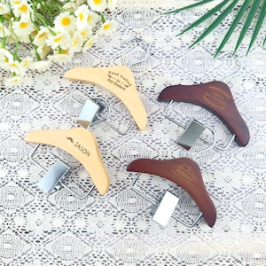 Op de afbeelding: Vier houten kledinghangers met metalen clips. Twee zijn van licht hout met tekst, een met "Hand Crafted by Jan Hudson" en de andere "~ JASON". De andere twee zijn van donker hout met tekst.