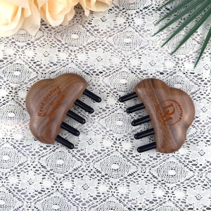 Könnte beinhalten: Zwei herzförmige Massage-Werkzeuge aus Holz mit schwarzen Zinken. Die Werkzeuge sind mit den Worten "Hand Crafted by Jan Hudson" und "Handcrafted by DM" graviert. Die Werkzeuge sind aus dunkelbraunem Holz gefertigt.