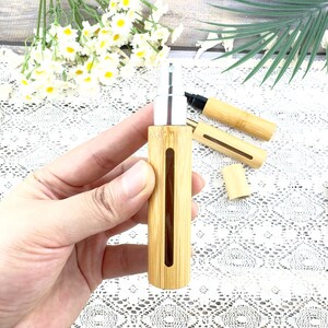 May include: A bamboo essential oil spray bottle with a silver top. The bottle has a rectangular shape with a vertical viewing window. The image also shows a bamboo cap and a black marker.