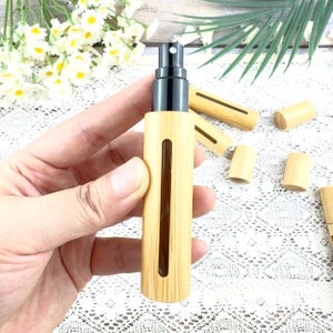 May include: A bamboo essential oil spray bottle with a black atomizer. The bottle has a rectangular window to view the contents. Several bamboo caps and spray bottles are scattered in the background.