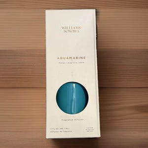 May include: A white rectangular box for a Williams Sonoma Aquamarine fragrance diffuser. The packaging features the text Williams Sonoma, Aquamarine, mango | magnolia | palm, and 3 fl oz (88.7 ml). A circular cutout reveals a bright blue bottle.