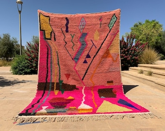 Puede incluir: Una vibrante alfombra tejida a mano con un fondo rosa coral y un diseño geométrico. La alfombra presenta formas abstractas coloridas en amarillo, azul, verde y negro. El borde inferior tiene flecos. Esta alfombra decorativa mide aproximadamente 200 cm x 300 cm.