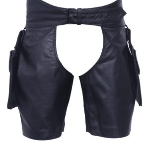 May include: Black leather chaps with a high waist and a belt closure. The chaps have a cutout design in the front and pockets on the sides. The leather appears to be smooth and the chaps are designed to be worn over other clothing.