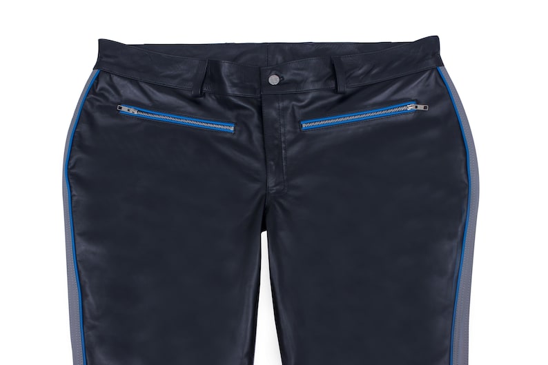 A close-up of the waist and upper thighs of black leather pants, showing two horizontal pockets with blue zippers.