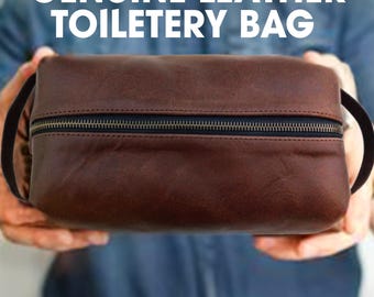 May include: A brown genuine leather wash bag with a black zip and handles. The bag is rectangular and features the text "GENUINE LEATHER TOILETRY BAG" in white.