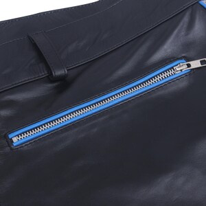 A close-up of the black leather pants, showing a diagonal pocket with a blue zipper.