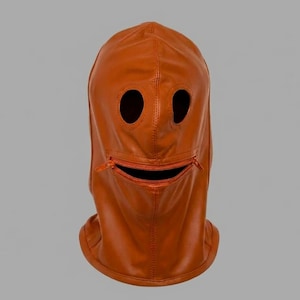 Peut inclure: Une cagoule en cuir orange brûlé dotée de deux ouvertures circulaires pour les yeux et d'une ouverture buccale horizontale zippée. Le couvre-chef présente des coutures verticales et horizontales visibles, offrant un aspect lisse et structuré.
