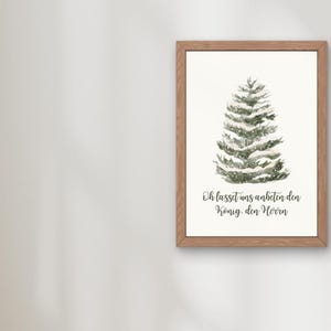 May include: A framed print featuring a watercolor illustration of a snow-covered evergreen tree. The artwork is set against a white background and framed in a light brown wooden frame. The text at the bottom reads, "Oh lasset uns anbeten den König den Herrn."