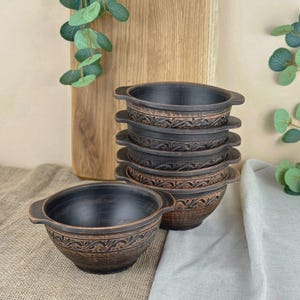 Peut inclure: Ensemble de six bols en céramique brun foncé avec des poignées et des motifs floraux décoratifs. Un bol est séparé. Les bols sont sur une surface en toile de jute.