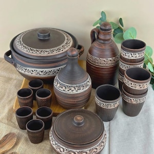 Peut inclure: Ensemble de vaisselle en céramique marron, comprenant une grande marmite avec couvercle, une bouteille, un petit pot, des verres à shot et des tasses. Chaque pièce présente un motif décoratif blanc et marron sur le bord.