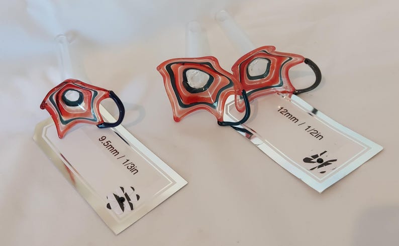 May include: Two abstract glass ornaments with red, black, and white patterns. One is labeled 9.5mm / 1/3in, the other 12mm / 1/2in. Each has a dark blue handle and a clear stem.