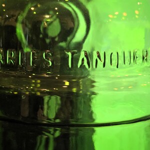 May include: Close-up of a green glass bottle with the embossed text "CHARLES TANQUERAY". The bottle has a rounded shape and a glossy finish, reflecting light. The overall theme is related to alcoholic beverages.
