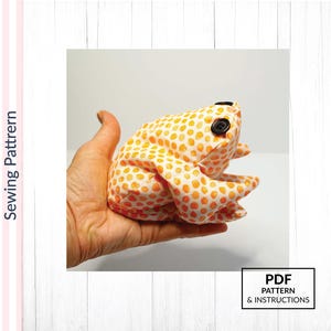 May include: A handmade frog plush toy in orange fabric with white polka dots. The frog has black button eyes and is held in a hand. The image includes the text "PDF PATTERN & INSTRUCTIONS".