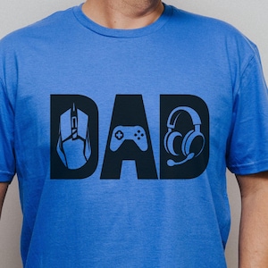 May include: A blue t-shirt with the word "DAD" in black, incorporating gaming symbols: a mouse, a game controller, and headphones. The short-sleeved shirt is made of a soft fabric.