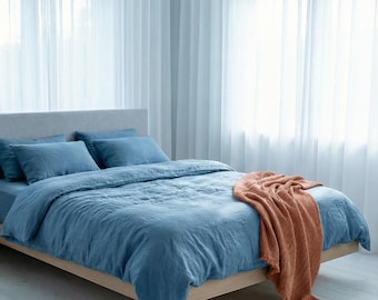 May include: A bed with blue bedding, including a duvet cover, fitted sheet, and pillowcases. A rust-colored throw blanket is draped over the bed. A potted plant in a woven basket sits beside the bed.