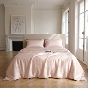 May include: A bed with light pink satin bedding, including a duvet cover and two pillowcases. The bed is made up and ready for use. The room has a neutral color palette with a framed art print and a fireplace.